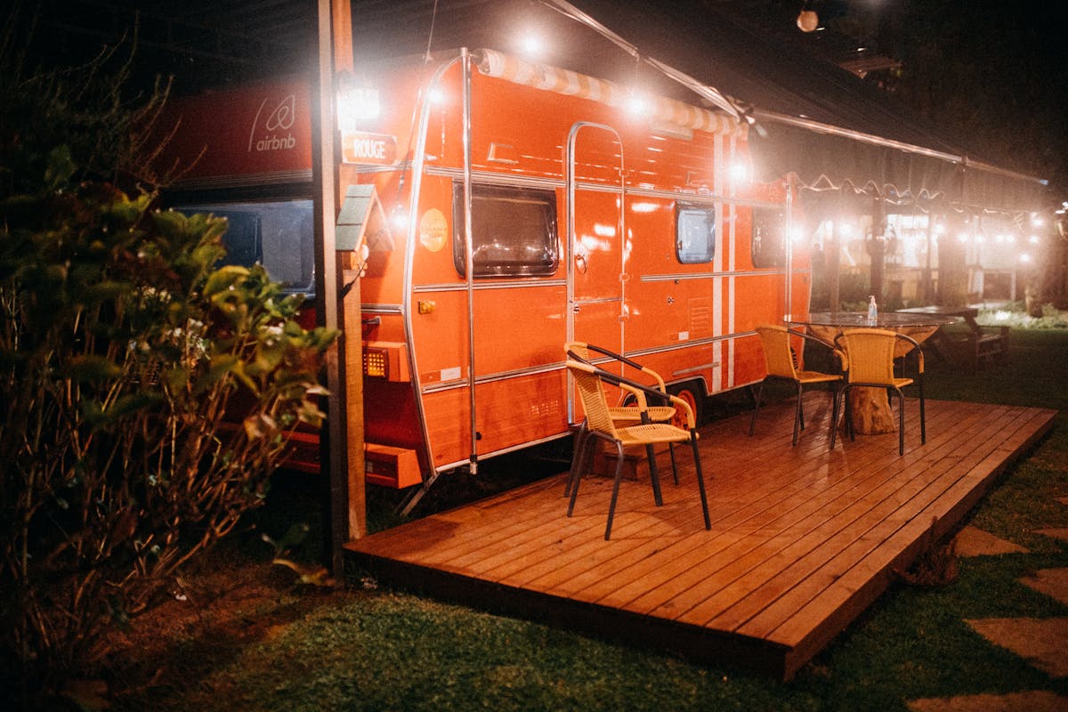 Orange camper trailer lit up with string lights at night, powered by an inverter running AC appliances from battery